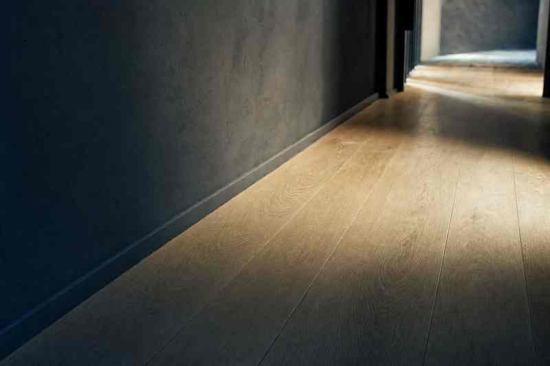 Een lege donkere gang met een houten vloer waarop licht valt